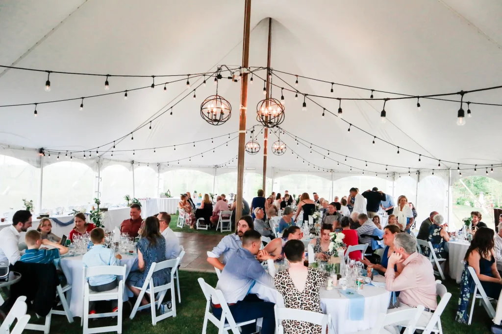 Event And Tent Rental Service-Calgary And Area 17 Inside a white event tent, guests gather at long tables under copper globe string lights for Ashley Zach’s celebration in Calgary.