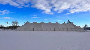 40 x 160 pole tent in winter with white canvas walls and a peaked roof standing over deep snow under a blue sky.