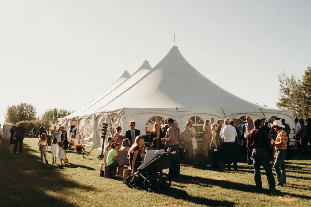 Wedding Tent Packages 17 A 40x80 white pole tent with open side walls, filled with guests gathering outdoors on a sunny day in Calgary.