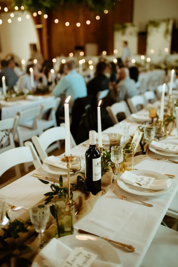 Event And Tent Rental Service-Calgary And Area 13 White table settings with tall candles, gold cutlery, glassware, and folded napkins arranged for a wedding reception atmosphere.