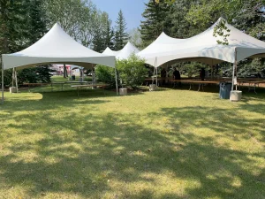 White modular Marquis tents on a sunny lawn with tables and guests gathered beneath arched canopy roofs and side walls.