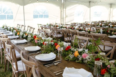 Event And Tent Rental Service-Calgary And Area 9 Rustic wooden wedding tables with colorful floral centerpieces, neatly set plates and cutlery, styled in neutral decor inside a pole tent.
