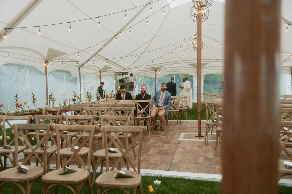 Wedding Tent Packages 13 Northern Light sailcloth tent interior with warm string lights and wooden ceremony seating, decorated with soft florals under a white canopy.