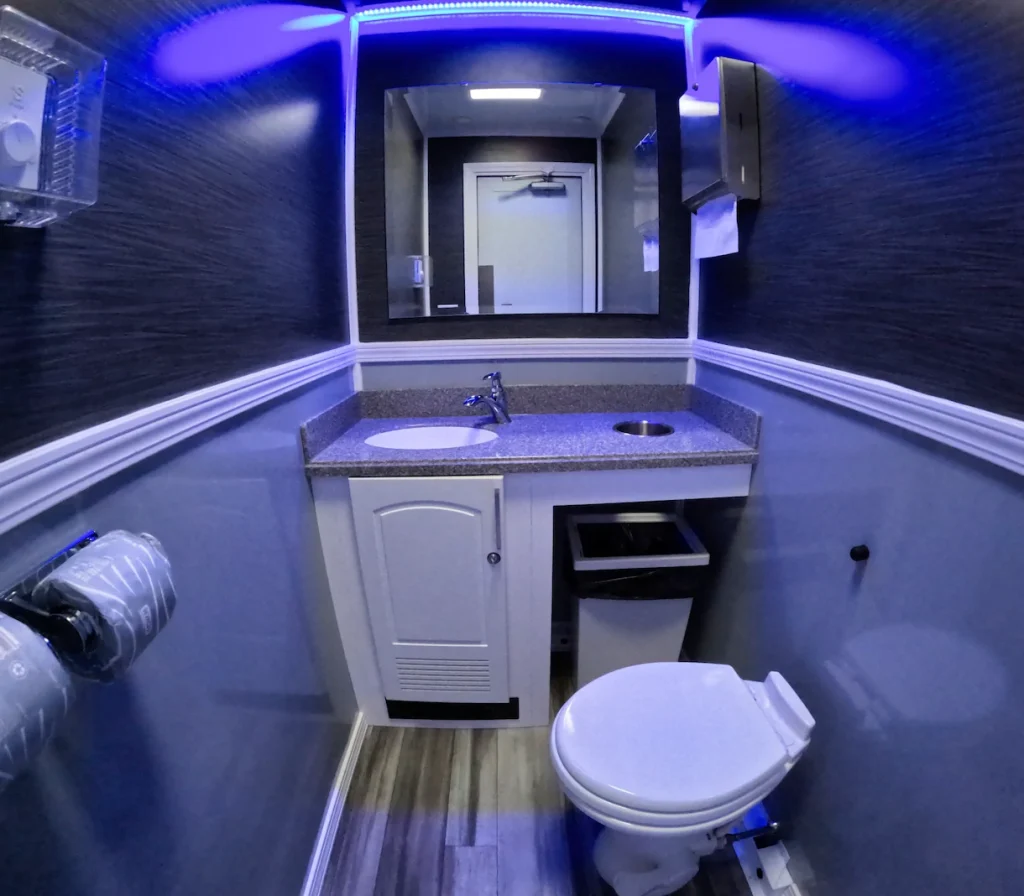 Inside the WR22 washroom trailer with blue LED lighting, a granite-style vanity, wall-mounted fixtures, and a toilet in a compact interior.