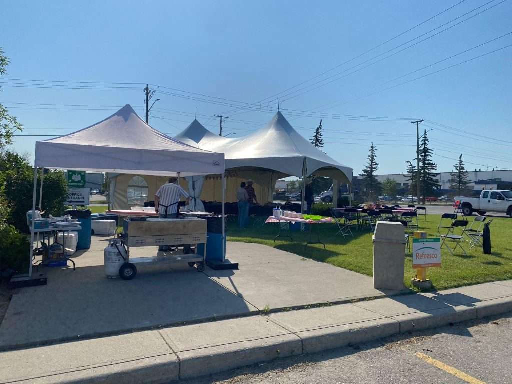 Commercial Pancake Griddle Rentals In Ab | Vibe Event Rentals 7 An outdoor Stampede breakfast setup in Calgary shows a commercial pancake griddle, tents, tables, and volunteers serving guests under clear skies.