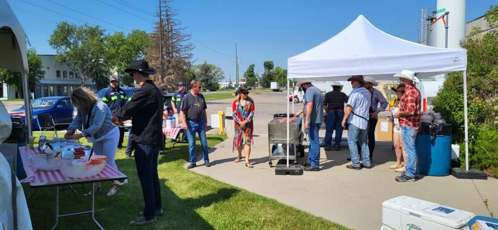 Commercial Pancake Griddle Rentals In Ab | Vibe Event Rentals 9 Guests gather around a commercial pancake griddle under a white canopy at an outdoor event in Calgary, while food is served beside the tent.